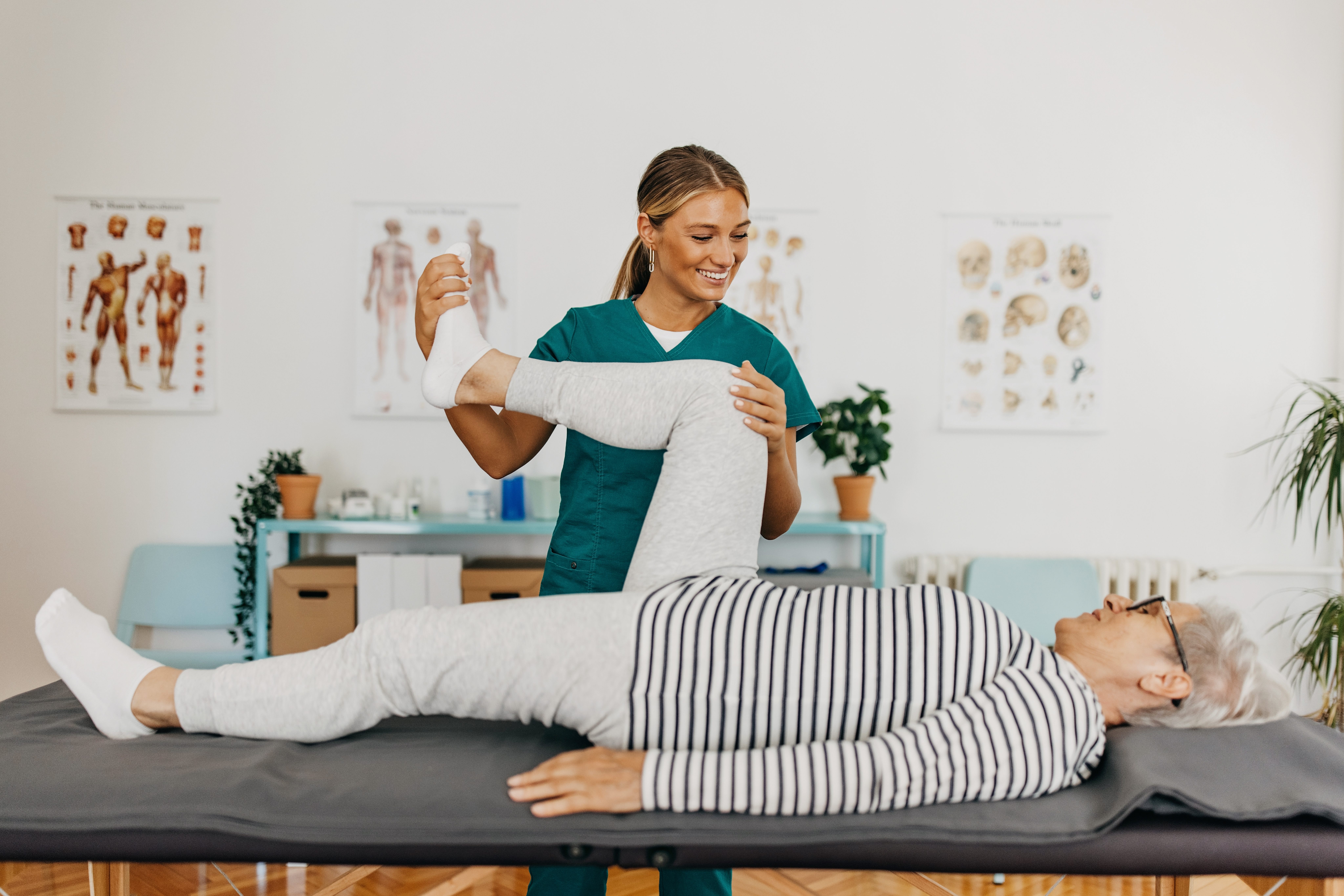 Senior lying on the medical table, exercising legs with assistance of the physiotherapist